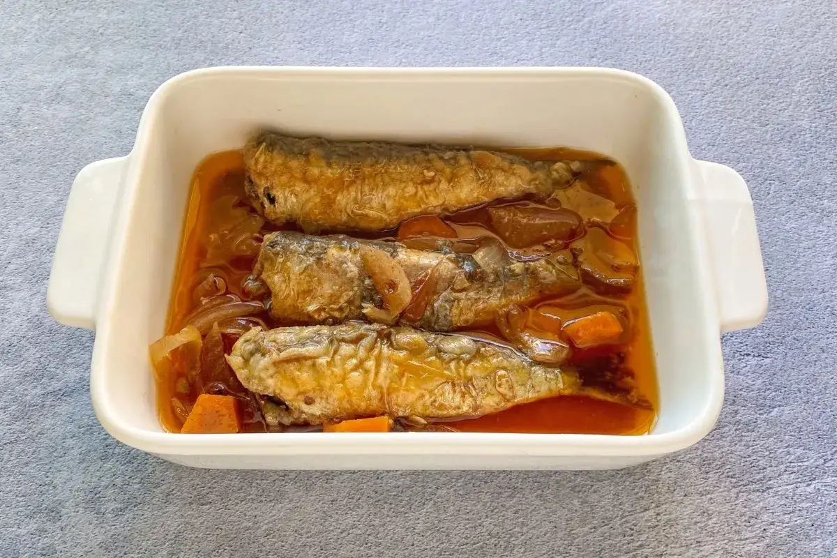 Tres sardinas en escabeche doradas y jugosas, nadando en una rica salsa con cebolla y zanahoria, listas para disfrutar.