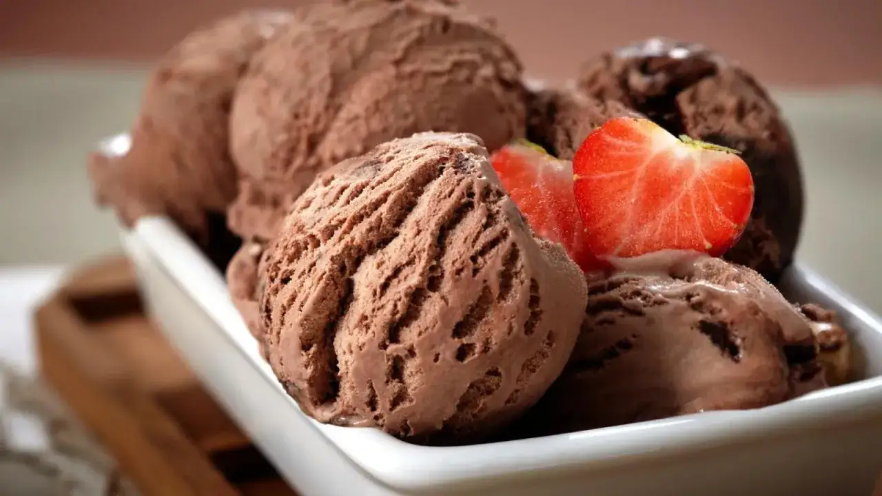 Un tazón blanco lleno de cremoso helado de chocolate casero, adornado con rodajas de fresa fresca.