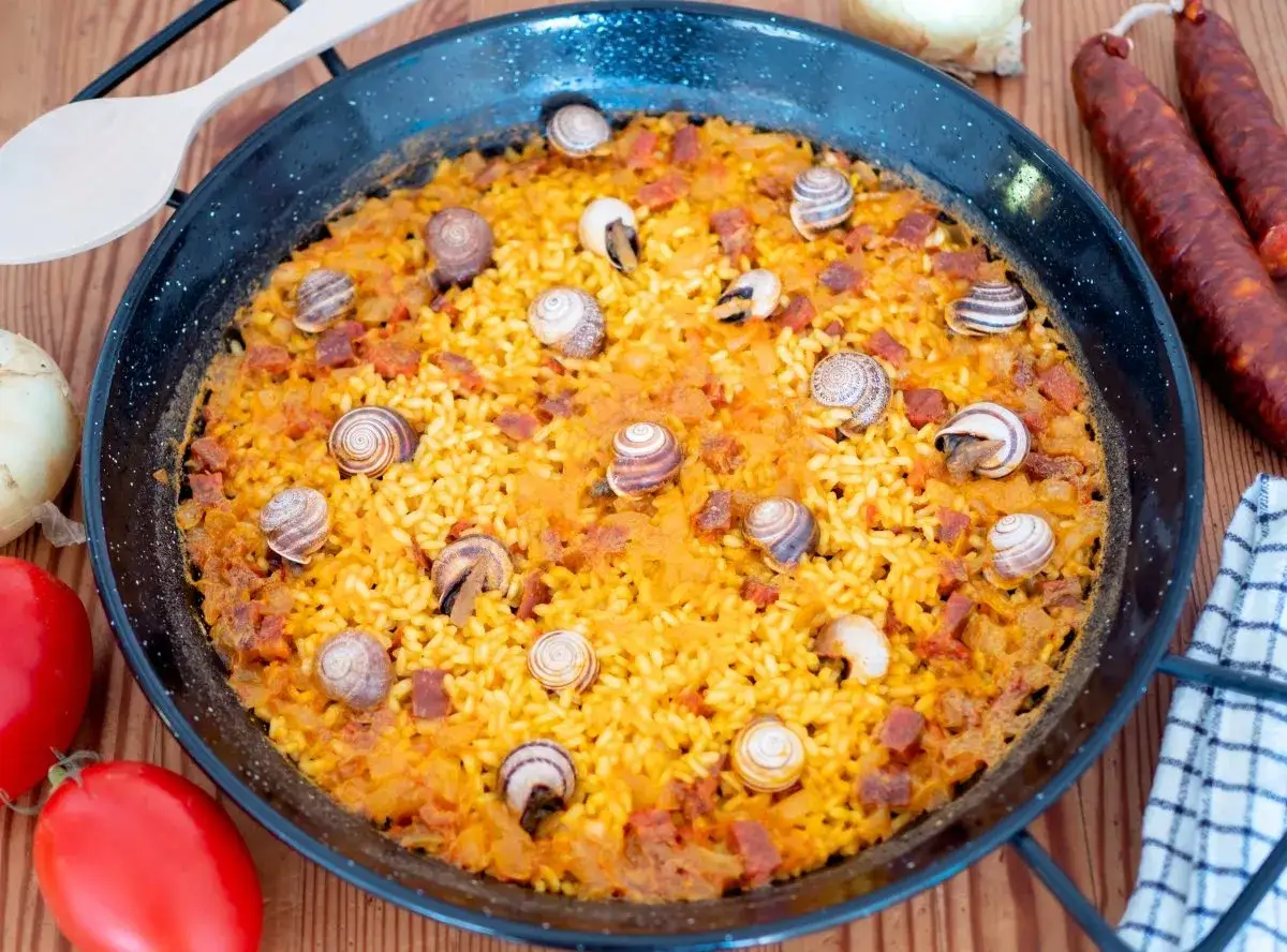 Arroz con caracoles, un plato tradicional espa&ntilde;ol, servido en paellera. El arroz amarillo est&aacute; salpicado de trozos de chorizo y caracoles.