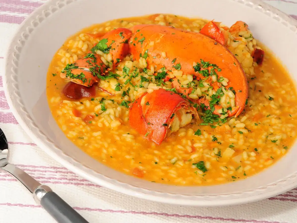Delicioso arroz caldoso con bogavante, adornado con perejil fresco. Un plato principal que evoca el sabor del mar.
