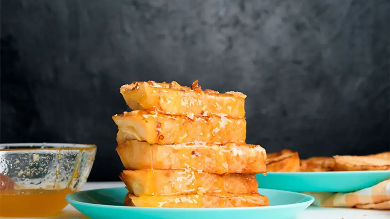 Torrijas de horchata doradas y jugosas, apiladas y bañadas en miel, con un cuenco de miel al lado.