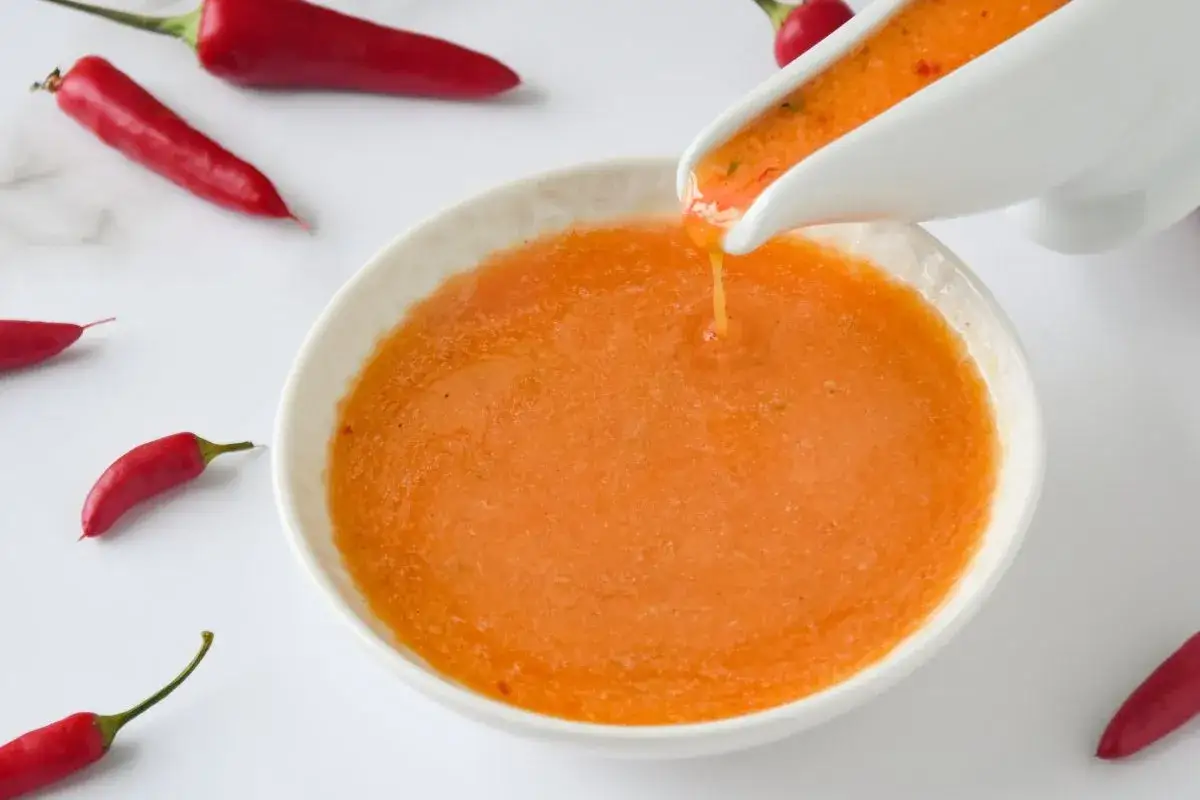 Salsa piri piri vertiéndose en un cuenco blanco, rodeada de chiles rojos frescos.