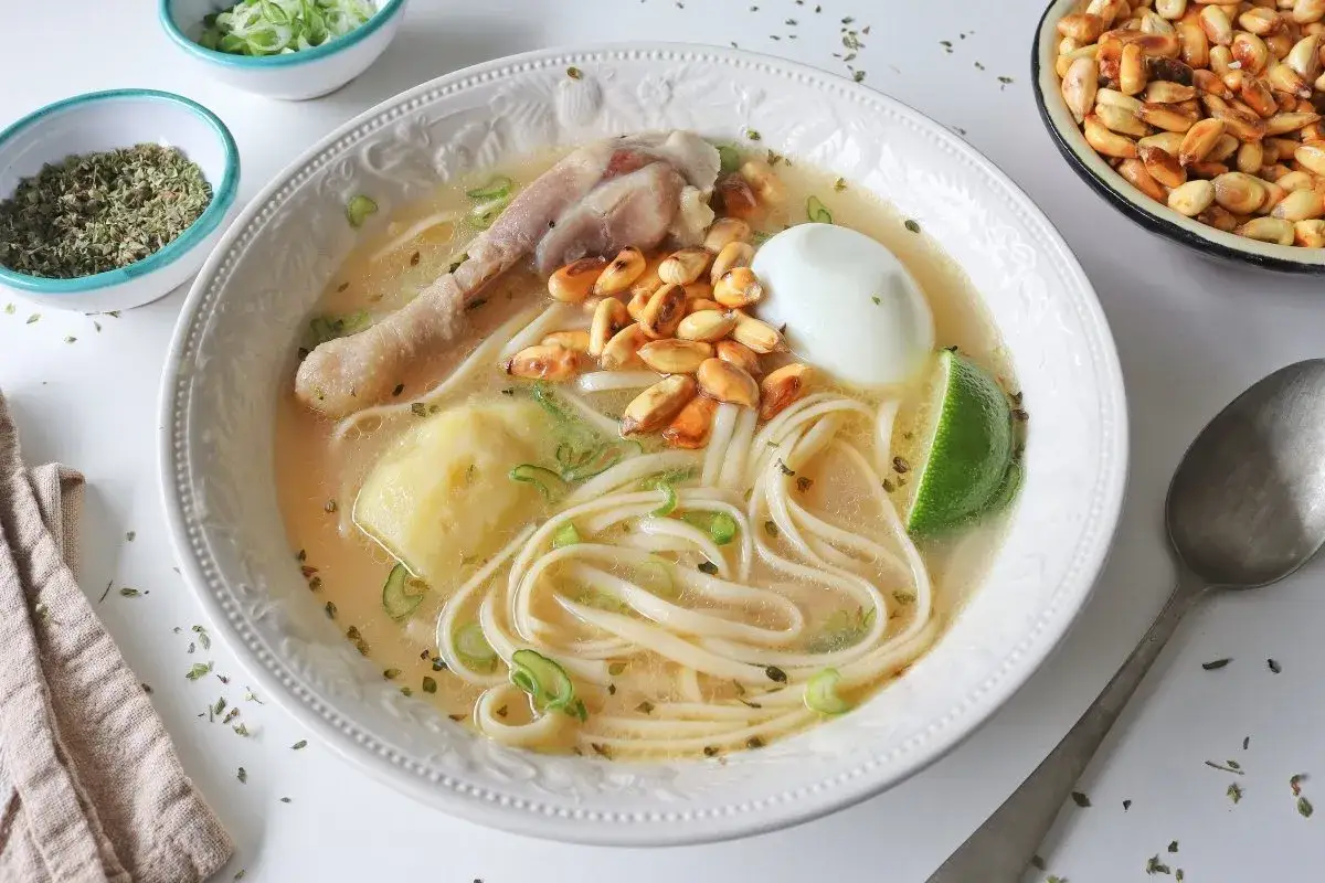 Un reconfortante caldo de gallina peruano con fideos, huevo duro, papa, choclo y un toque de limón.