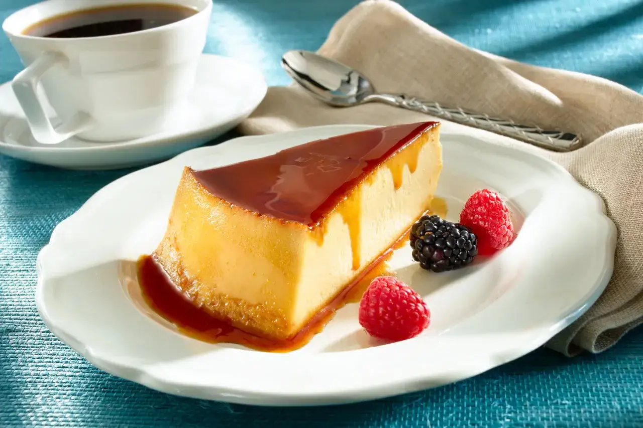 Un delicioso flan de queso con caramelo, acompañado de frambuesas y moras, junto a una taza de café.
