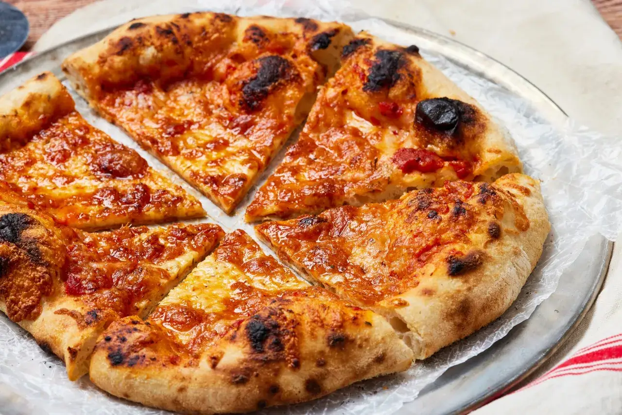 Pizza casera recién horneada, con bordes dorados y burbujeantes, cubierta de queso derretido y salsa de tomate.