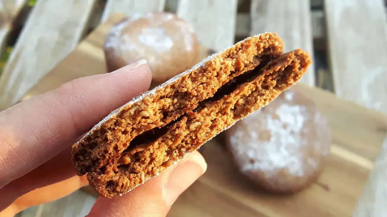 Galletas de avena crujientes, espolvoreadas con azúcar glas. Una mano sostiene una galleta partida, mostrando su interior.