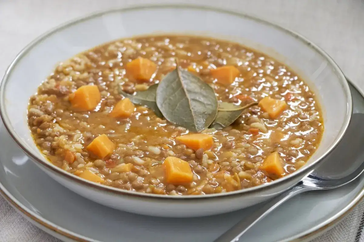 Un plato humeante de lentejas con arroz, trozos de calabaza y hojas de laurel.