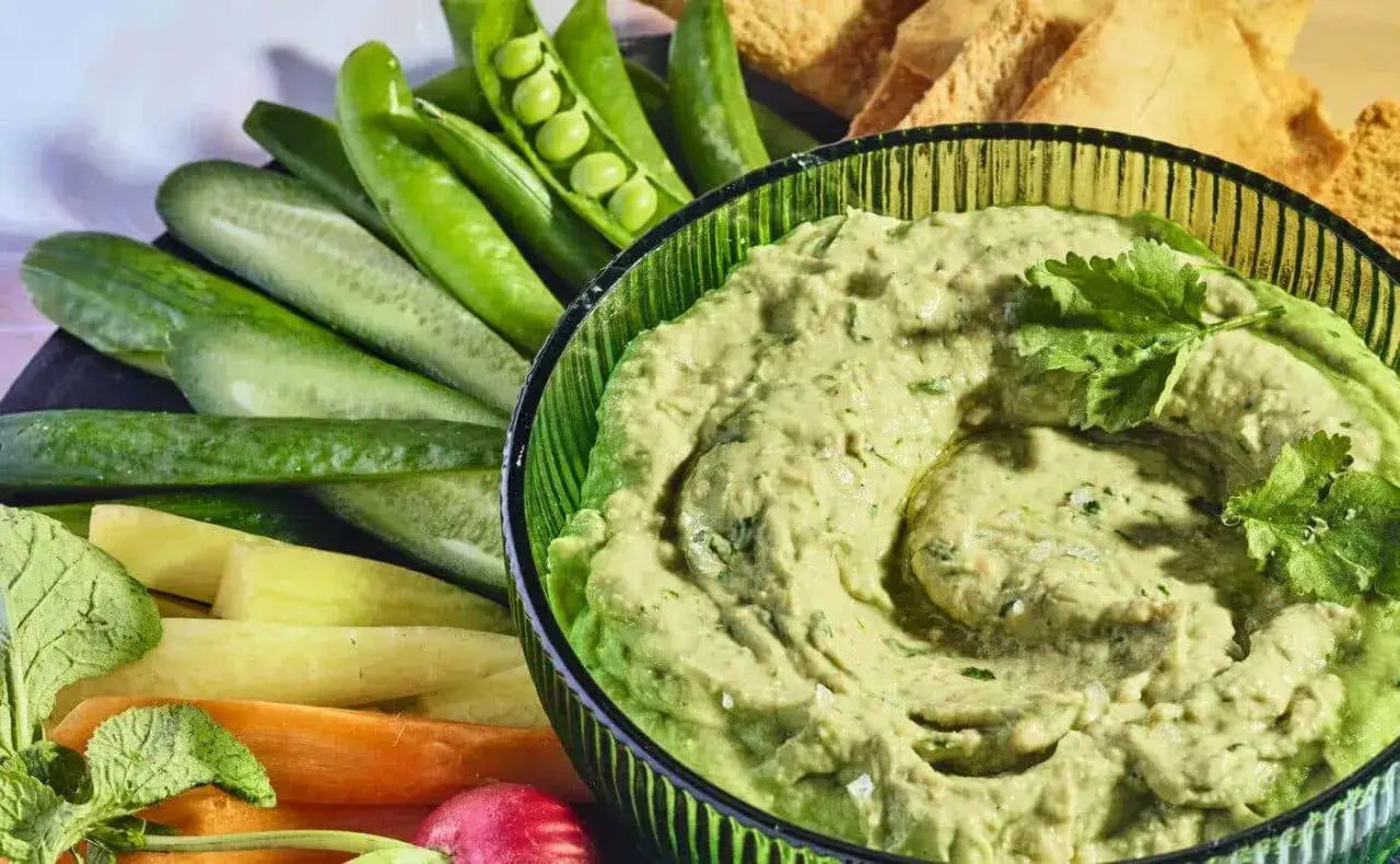 Un cremoso hummus de aguacate servido con crudit&eacute;s de pepino, zanahoria, r&aacute;bano y guisantes, acompa&ntilde;ado de pan de pita tostado.