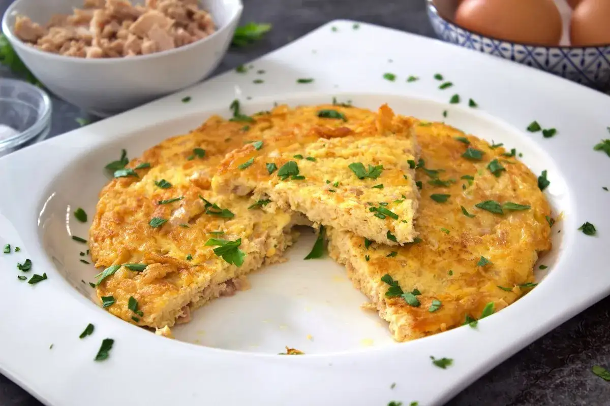 Tortilla de atún dorada y esponjosa, cortada en porciones y espolvoreada con perejil fresco. Un plato sencillo y delicioso.