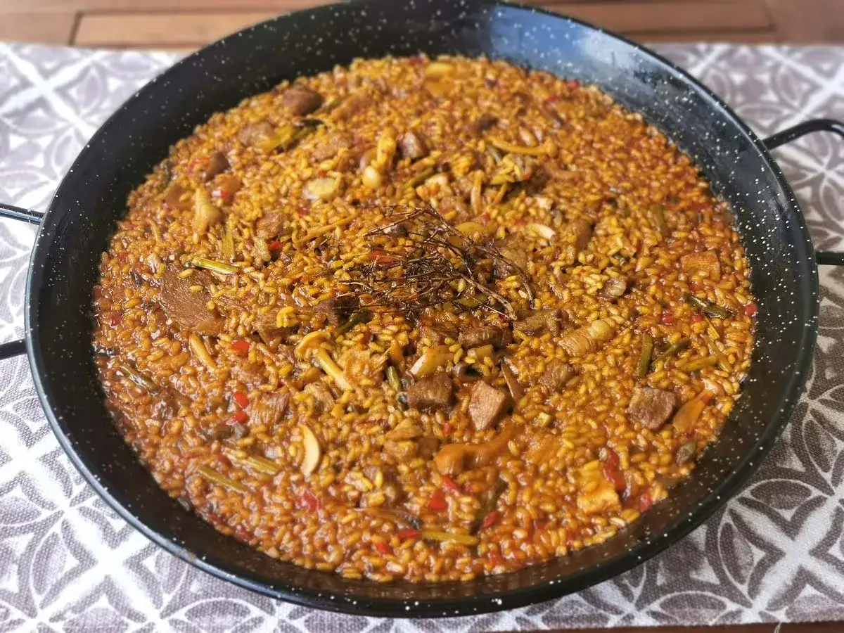 Paella de secreto, un plato de arroz dorado con trozos de carne de cerdo, pimientos rojos y judías verdes, coronado con tomillo fresco.
