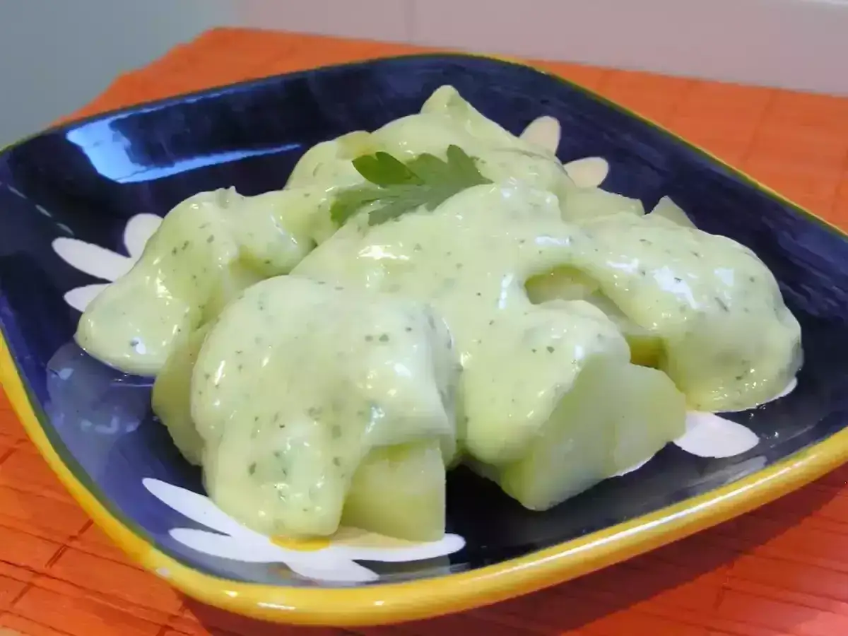 Patatas cubiertas con una cremosa salsa de ajo y perejil, servidas en un plato azul y blanco.