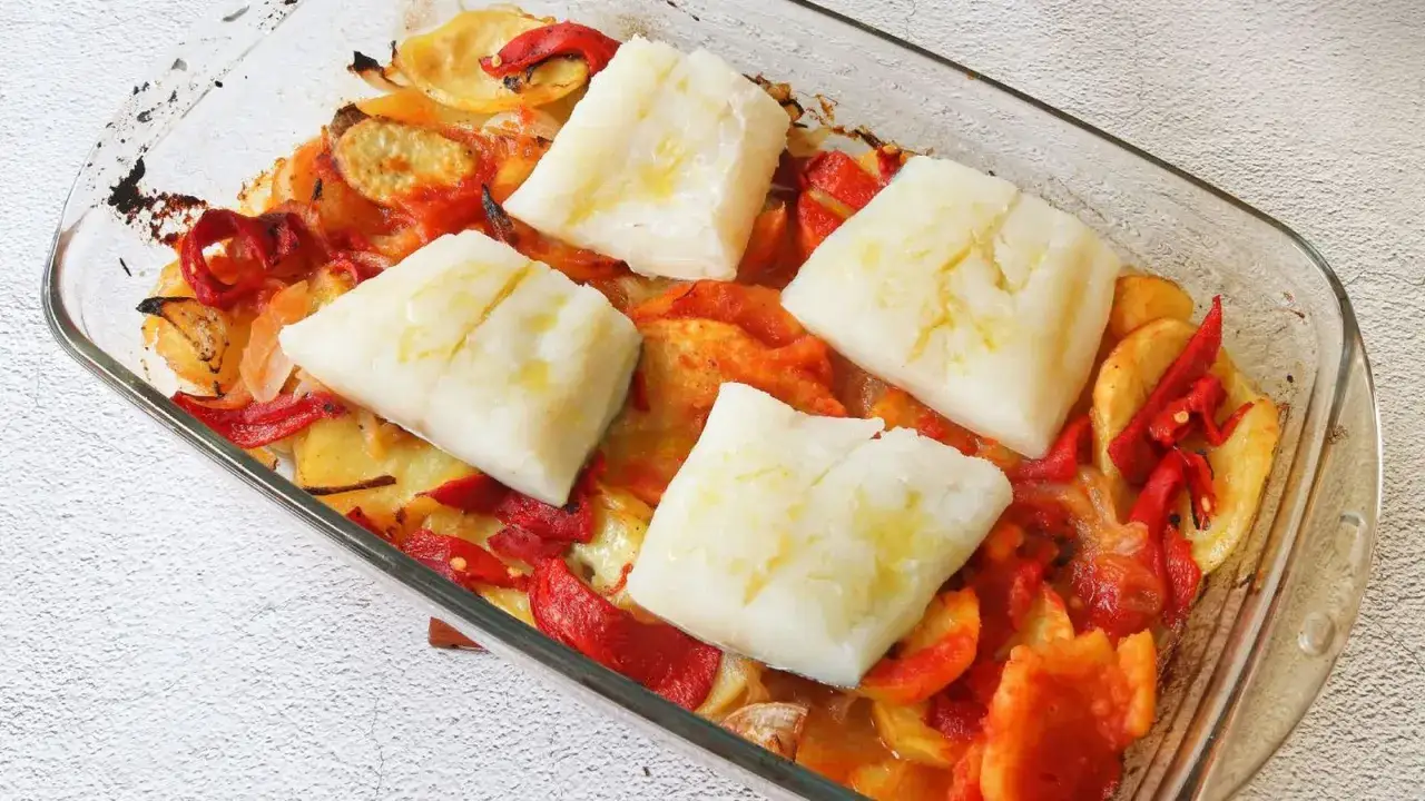 Bacalao al horno con patatas, pimientos rojos y cebolla en una fuente de cristal.