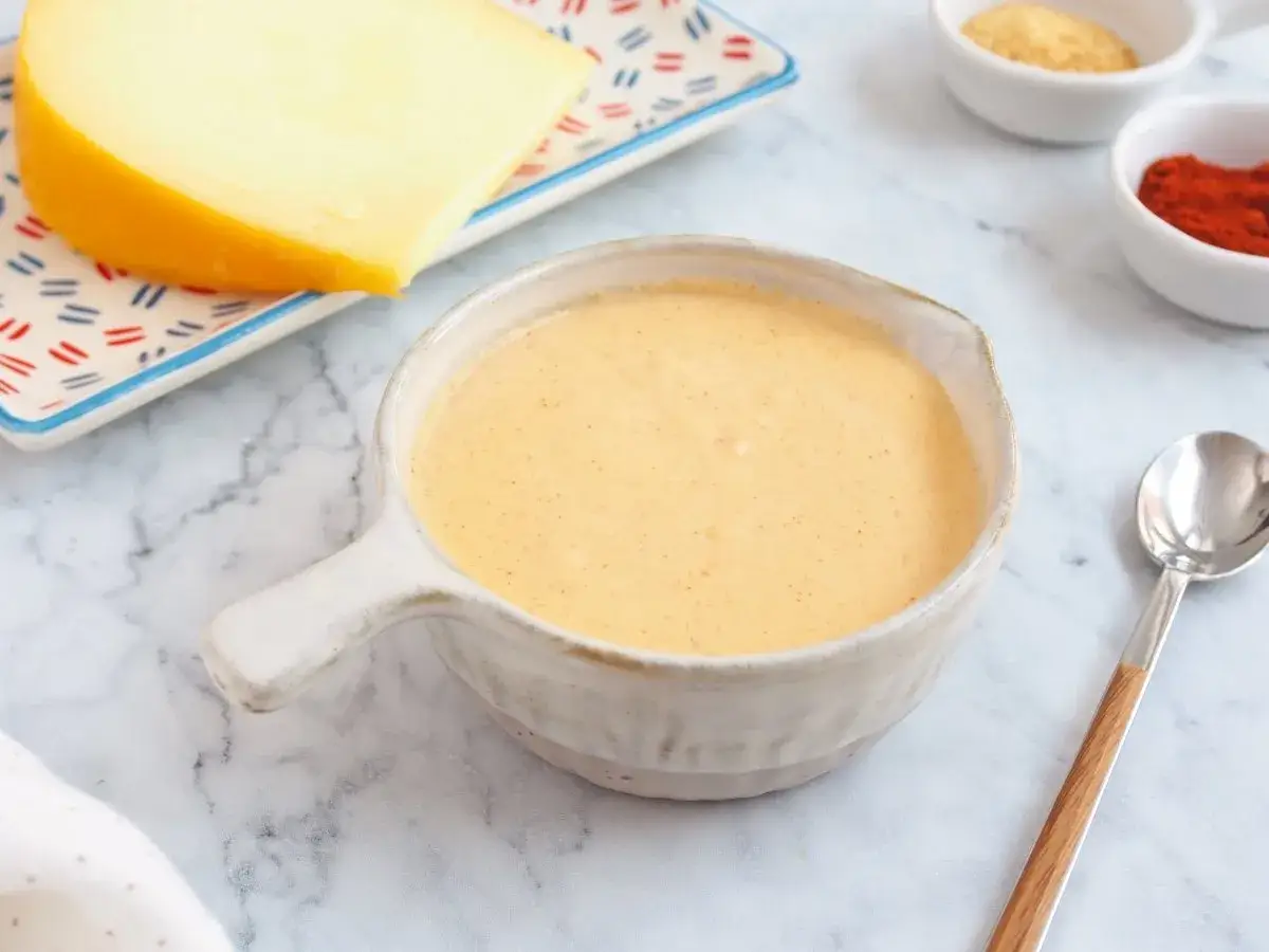 Crema de salsa de queso lista para servir, acompañada de un trozo de queso y especias.