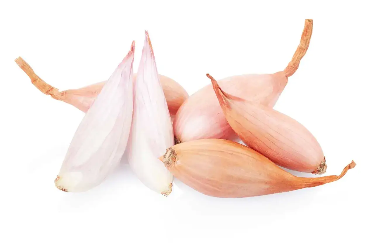 Un grupo de chalotas, algunas con piel rosada y otras peladas mostrando su interior blanco y rosado.
