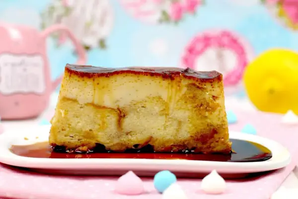 Un trozo de pan de calatrava con caramelo líquido sobre un plato blanco, adornado con merengues de colores y un limón al fondo.