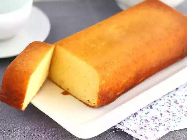 Un delicioso bizcocho de leche condensada, dorado y esponjoso, servido en una bandeja blanca con una porción cortada.