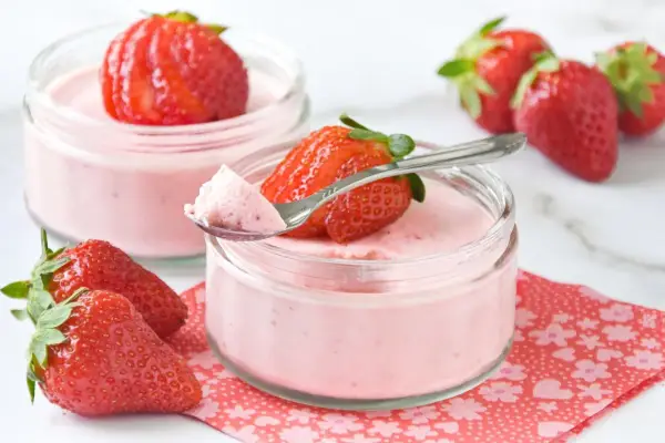 Delicioso mousse de fresa en vasitos, decorado con fresas frescas y una cucharita lista para probar.
