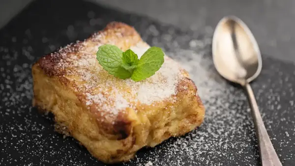 Torrijas con pan brioche, espolvoreadas con azúcar y decoradas con menta. Una cuchara plateada acompaña este delicioso postre.